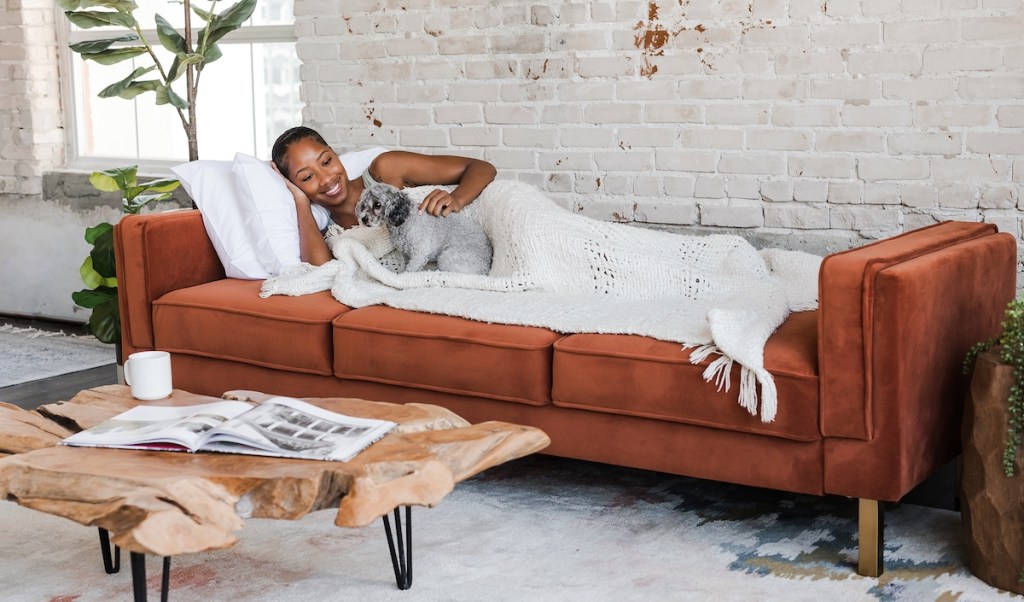 woman laying on rust colored sleeper sofa couch in industrial room with white brick