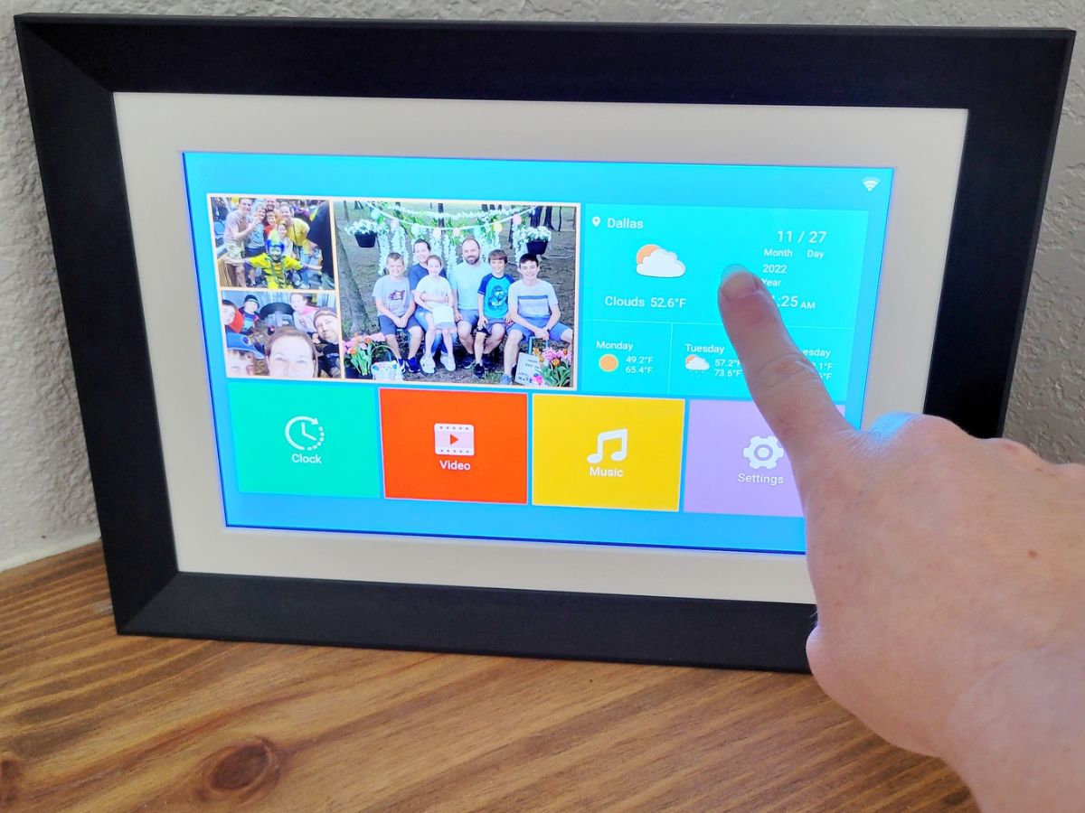 finger tapping screen on a digital photo frame displaying photos, the weather and other functions