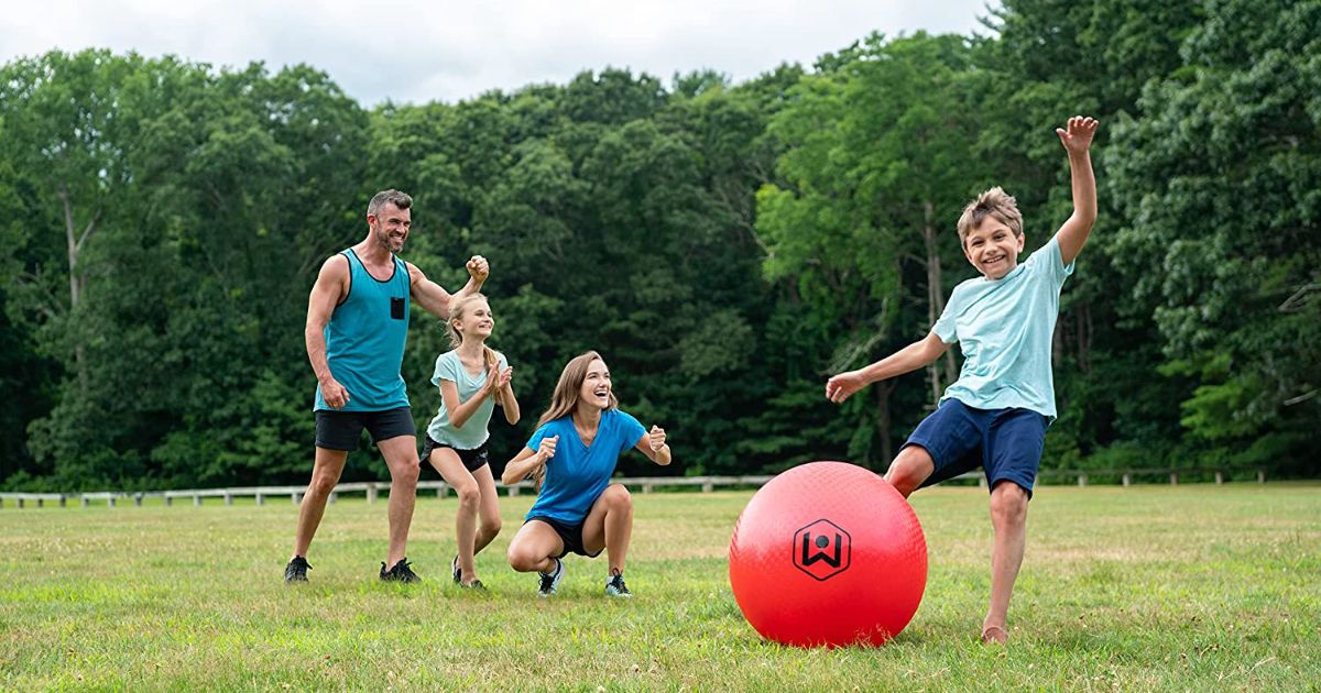 A family playing with an oversized red kickball in an open grassy field