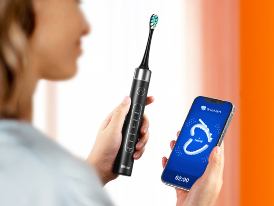 woman holding smartphone and electric toothbrush