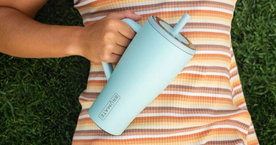 Woman laying in the grass holding a Brumate Era Tumbler 