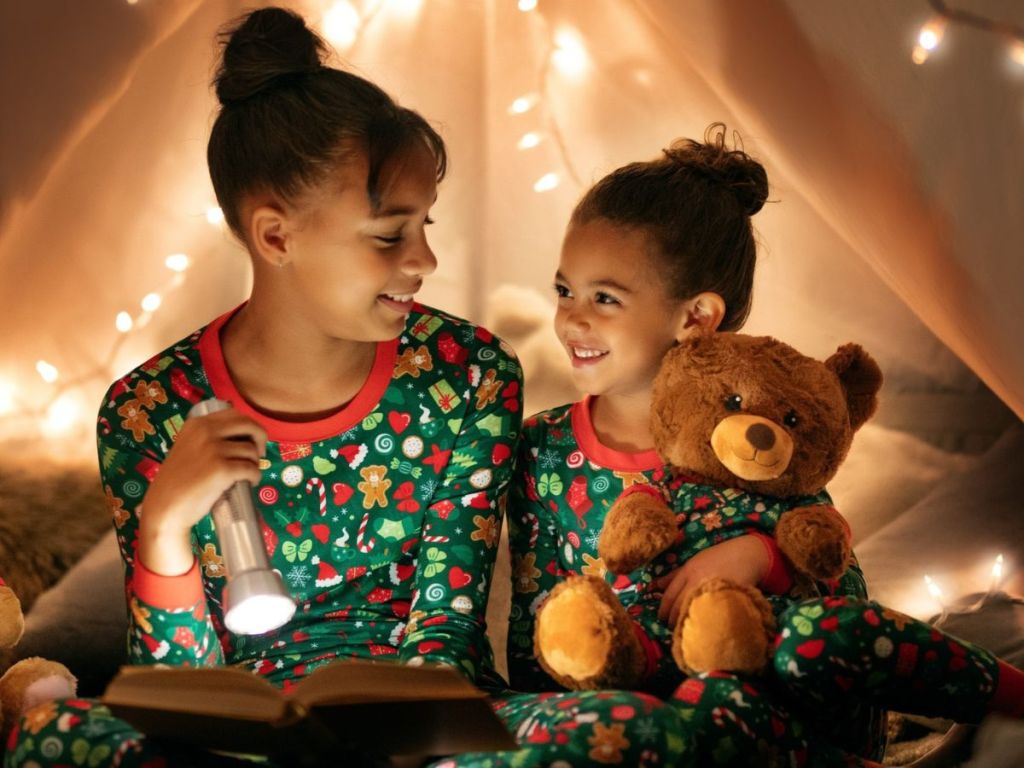 Two girls reading a book in a tent while wearing matching pajamas
