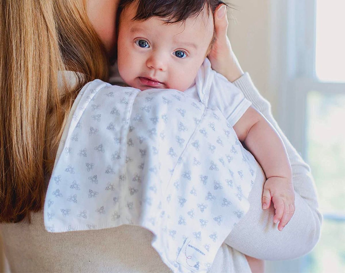 a baby resting on mom's shoulder with a Burts bees baby burp cloth 