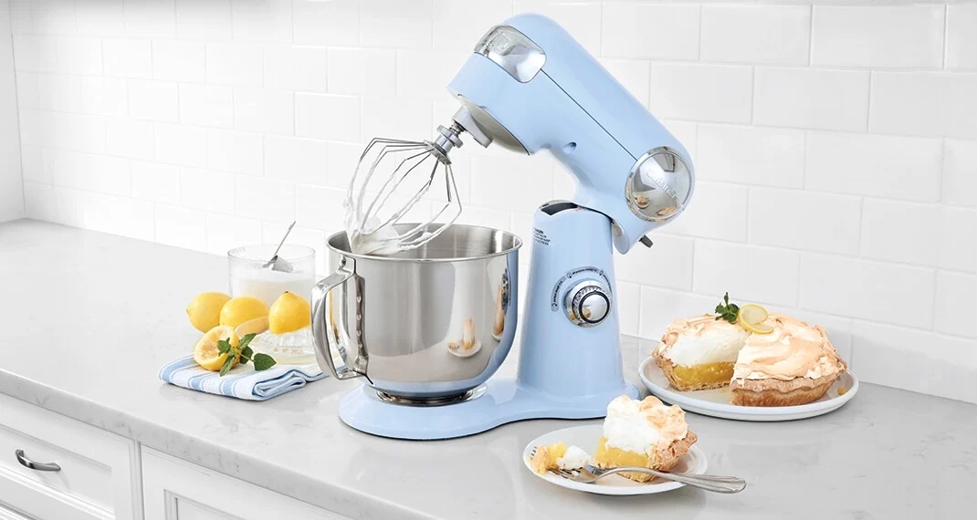 blue Cuisinart stand Mixer on a counter with lemons, a towel, a lemon pie, and a slice of pie on a plate with fork