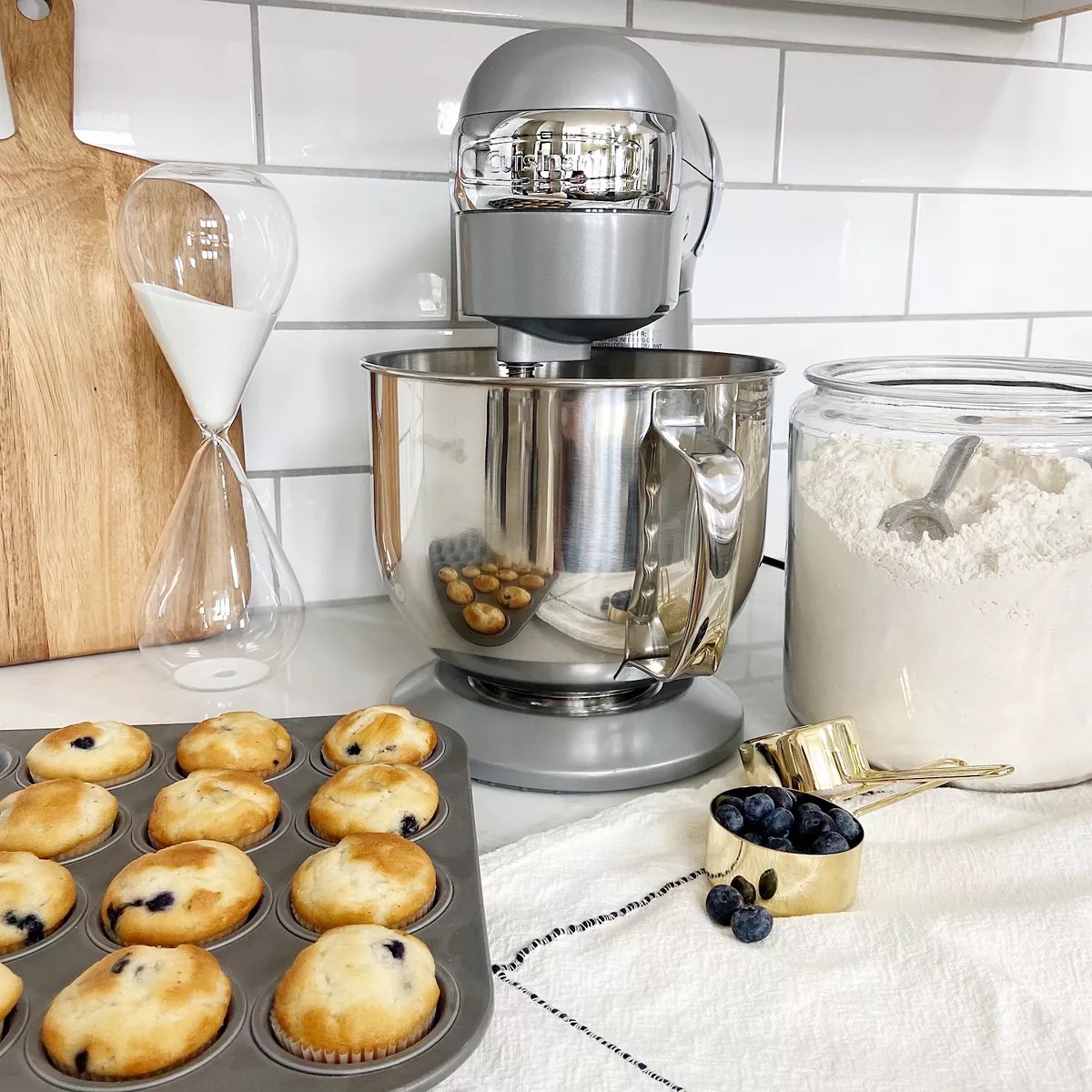 Cuisinart stand Mixer on a counter with a jar of flour, a cup of blueberries, and a pan of muffins
