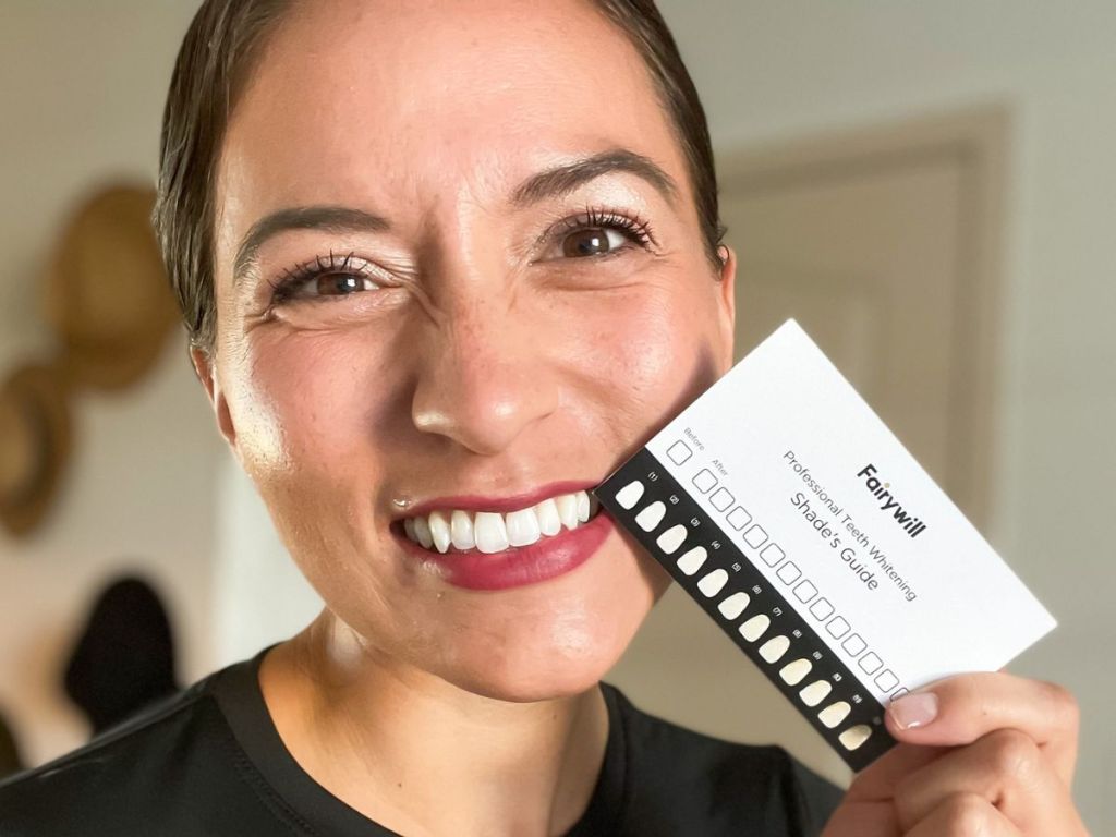 woman smiling holding teeth whitening chart next to her teeth