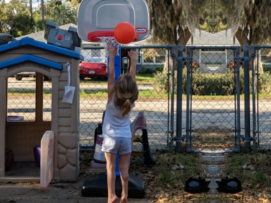 Toddler girl shooting basketball into little tikes basketball hoop outside