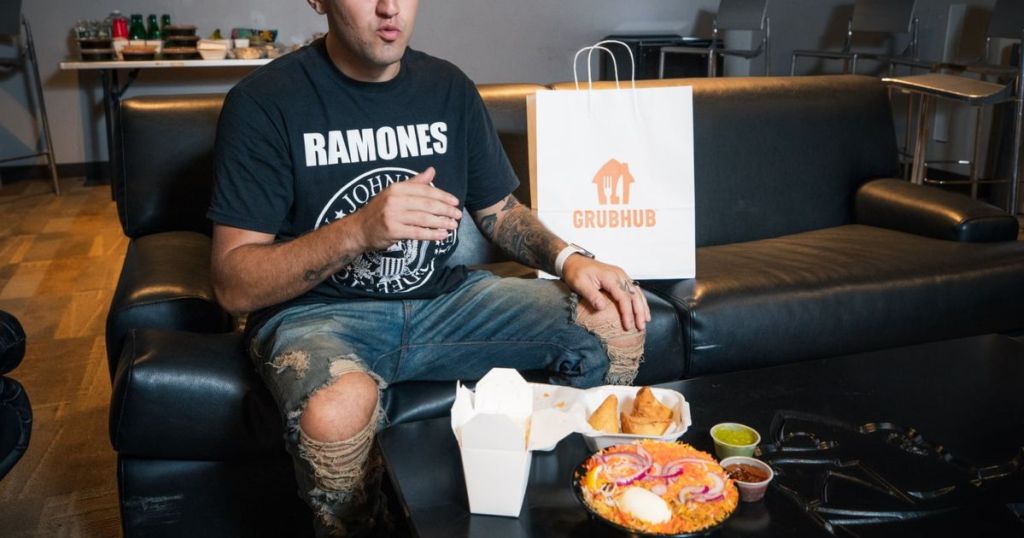 man with takeout sitting on couch next to a Grubhub bag