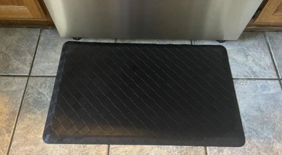 a black ergonomic floor mat in front of a stove kitchen cabinets