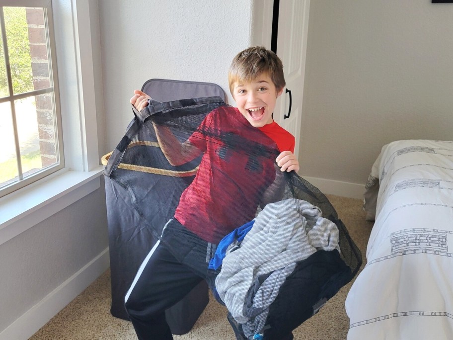 Boy smiling at the camera while holding a removable laundry hamper bag.