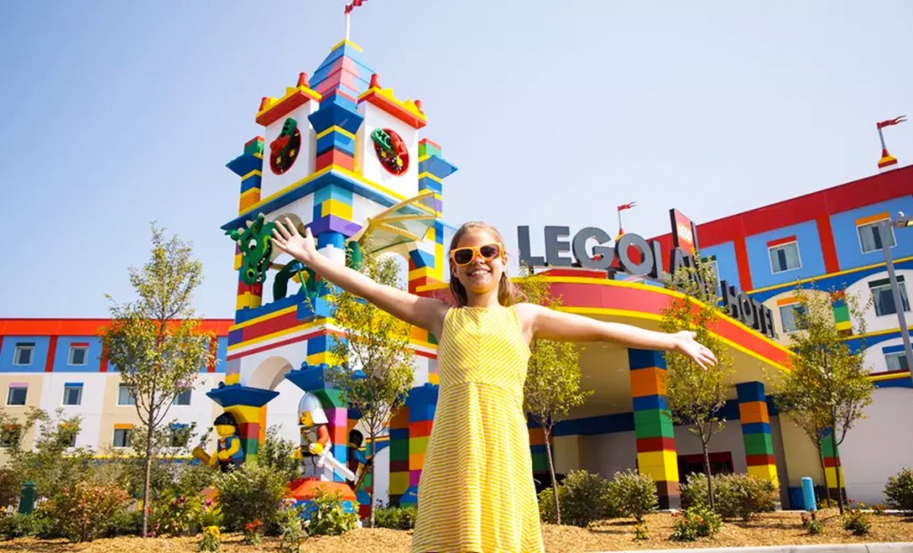 girl in yellow dress and sunglasses standing in front of legoland hotel