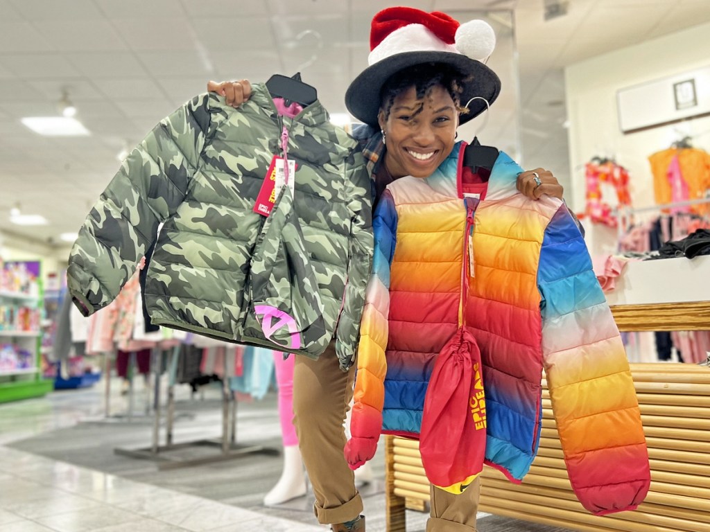 woman holding up two kids puffer jackets in store