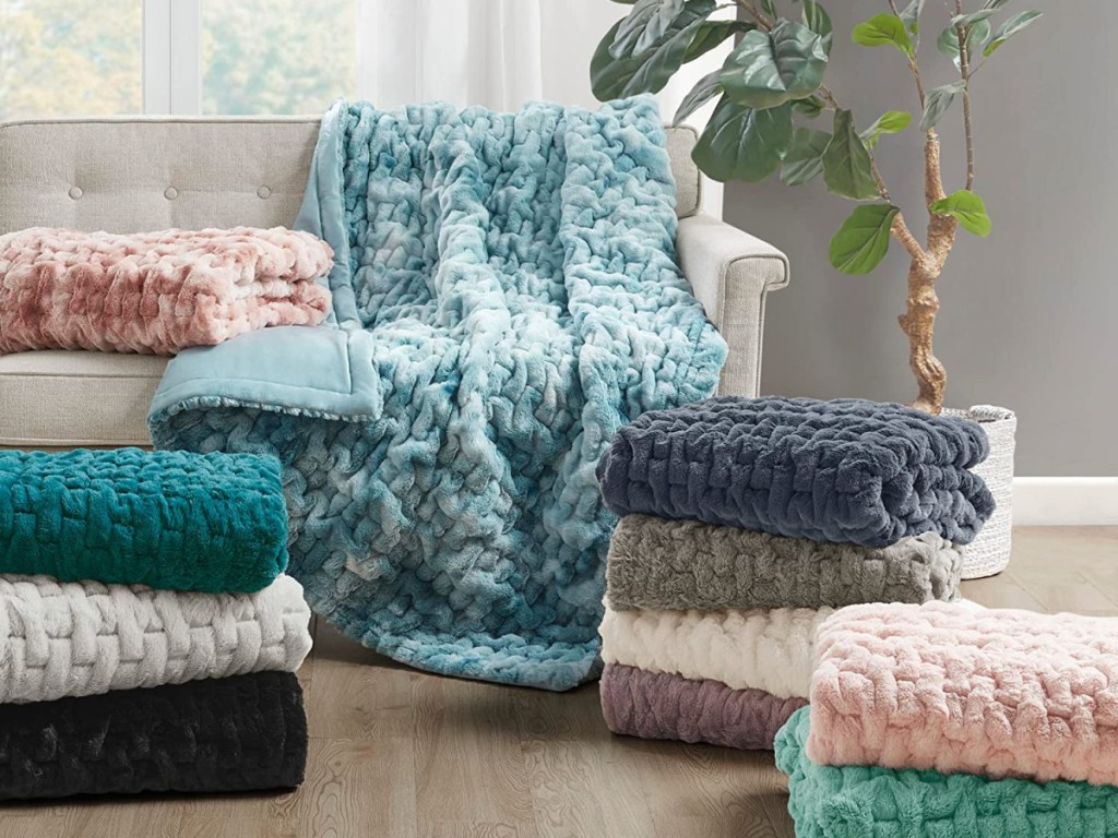 various Madison Park Ultra Soft Ruched Faux Fur Throws laying on a couch and stacked on the floor