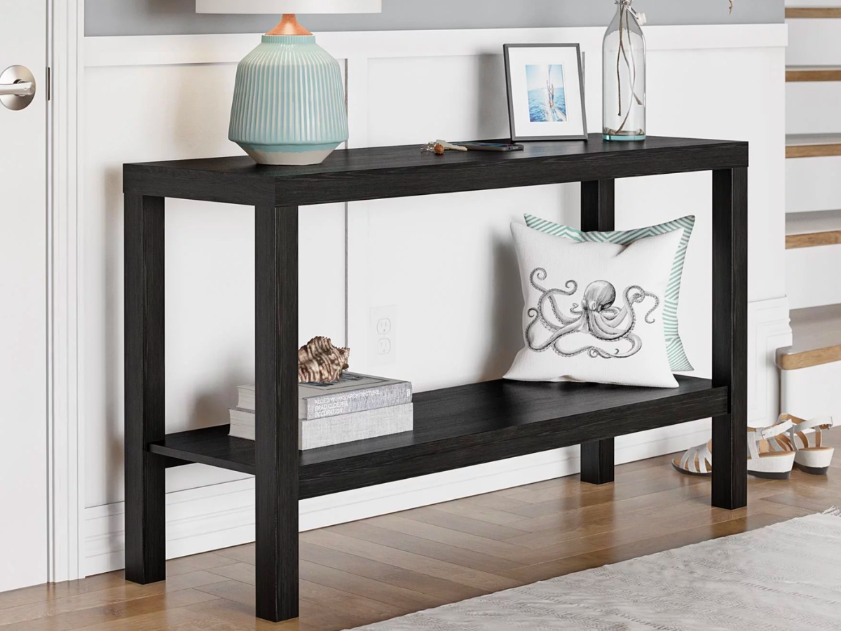 black console table with lamp, photos, and pillows on it