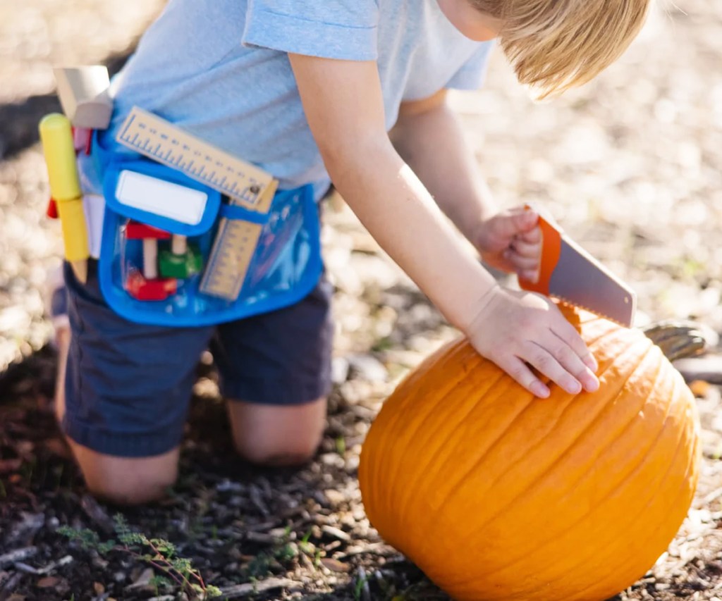 boy using toy saw on pumpkin