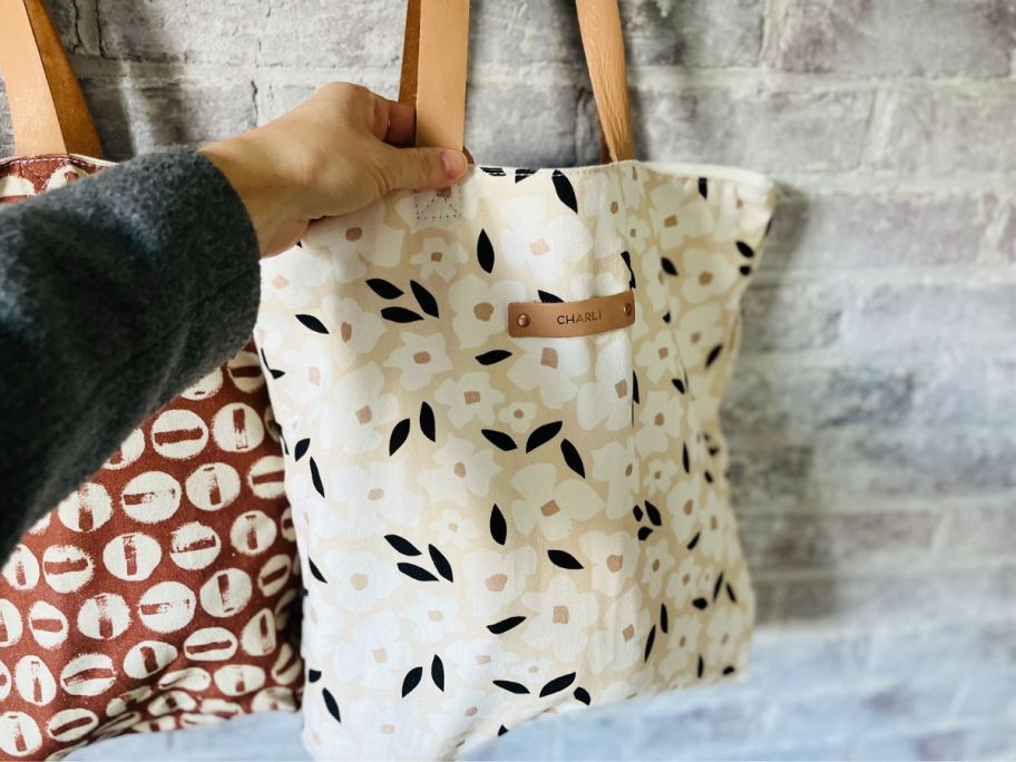Minted snap tote hanging on peg with woman's hand touching the top of the bag