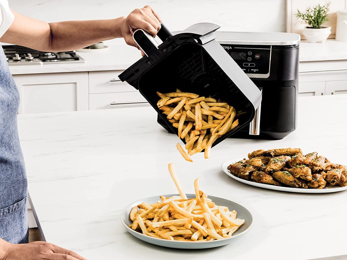 person pouring french fries from air fryer basket onto plate of fries