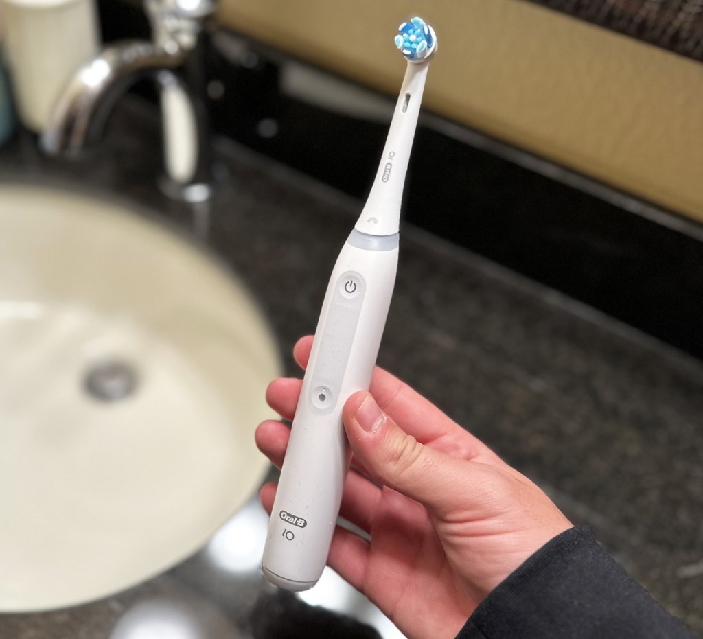 hand holding white electric toothbrush near sink