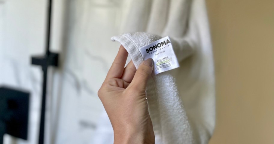 hand holding up tag on a sonoma goods for life bath towel hanging in bathroom