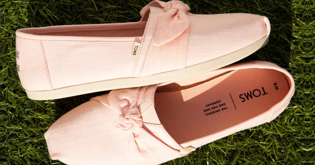 pair of pink toms shoes with bows in grass
