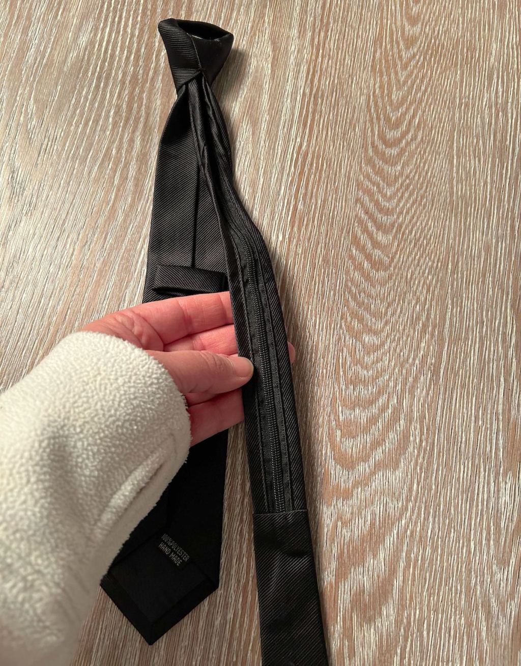 hand holding black tie on wood floor