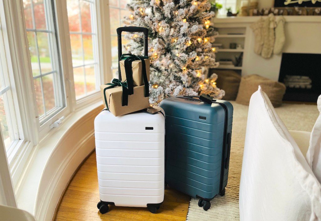 white and blue away suitcase in front of christmas tree with gifts