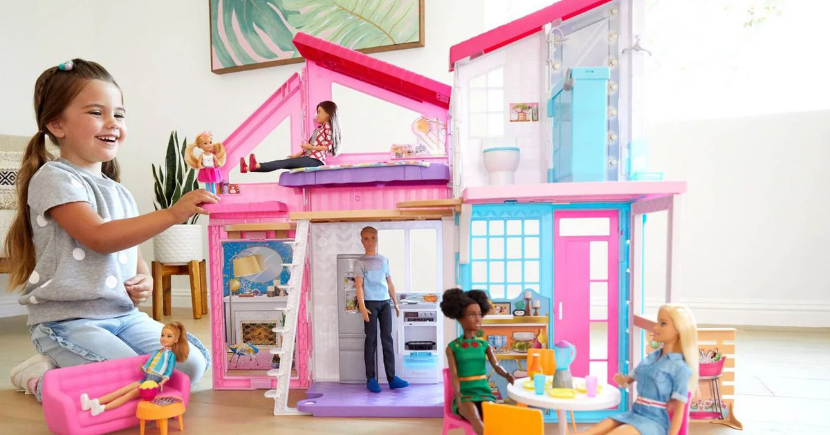 smiling girl playing with the barbie malibu house and accessories in a brightly lit room