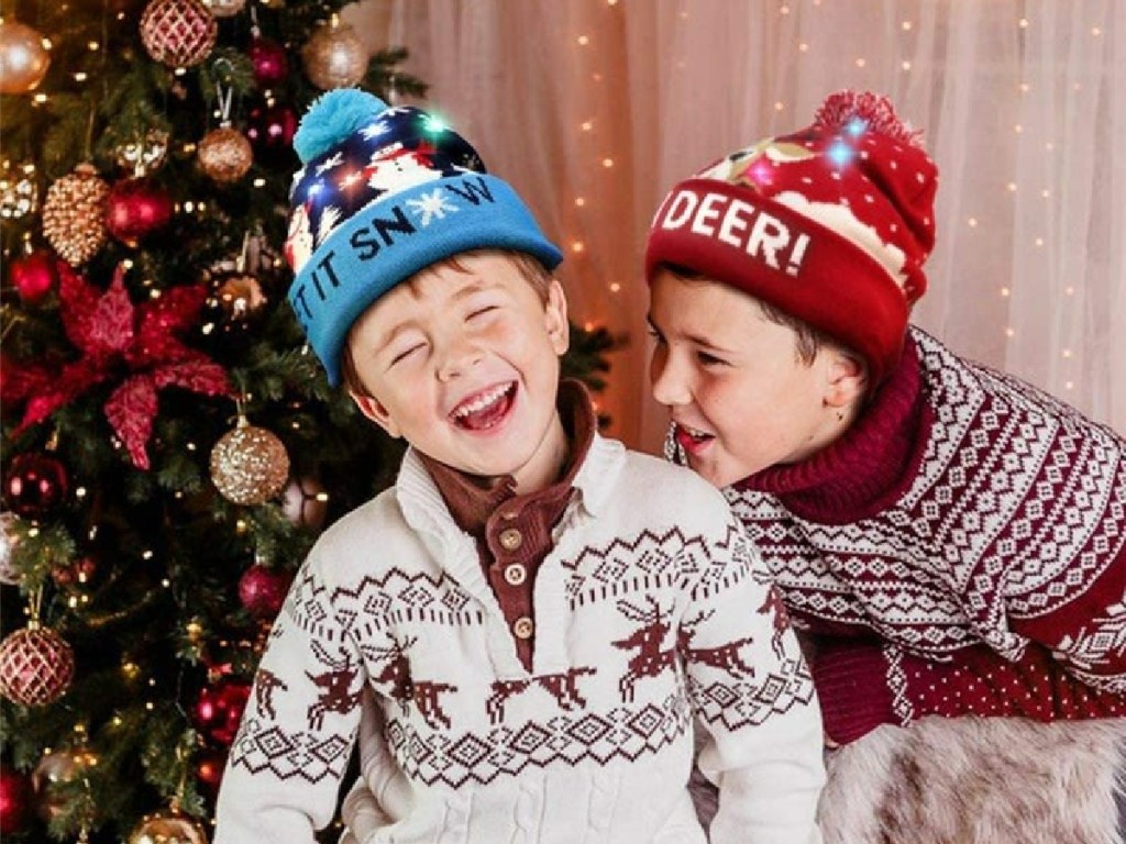 two laughing boys in front of a christmas tree wearing christmas led hats