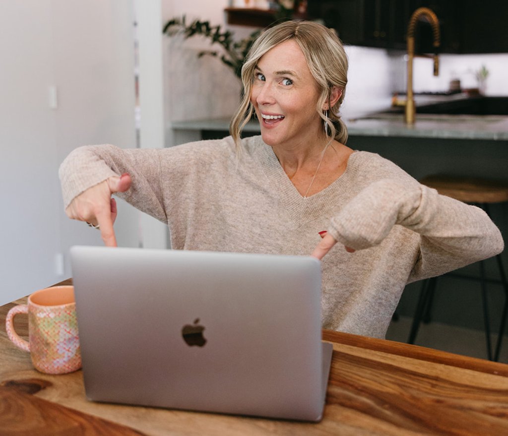 woman sitting at wood table pointing to apple laptop