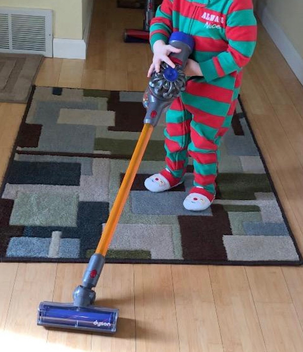 toddler pushing toy dyson vacuum cleaner on wood floor