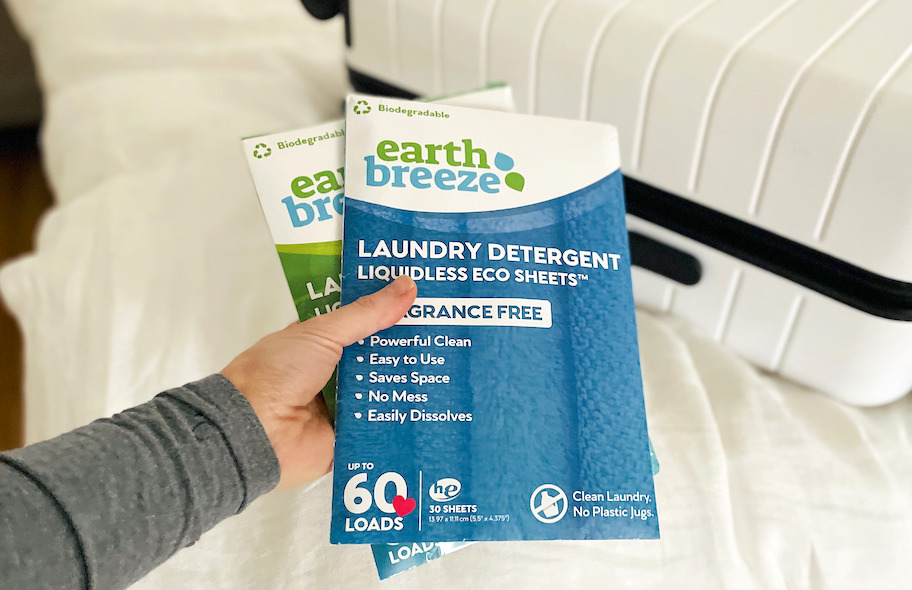 hand holding two packs of earth breeze laundry strips in front of white suitcase