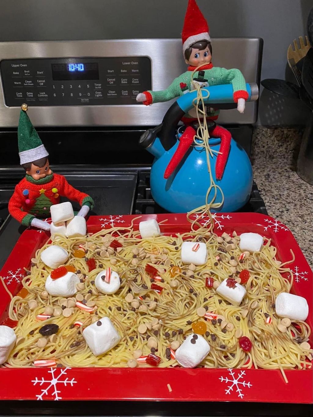 two elves on stove with huge platter of candy pasta
