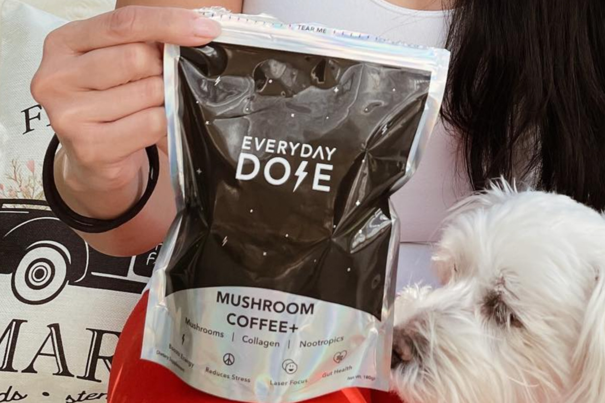 woman holding mushroom coffee pouch next to dog