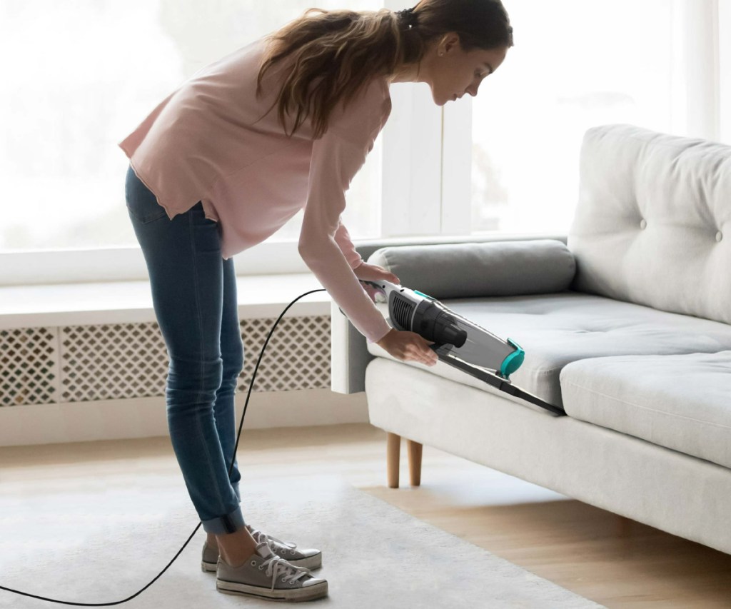 woman vacuuming under couch cushion with an ionvac stick vacuum