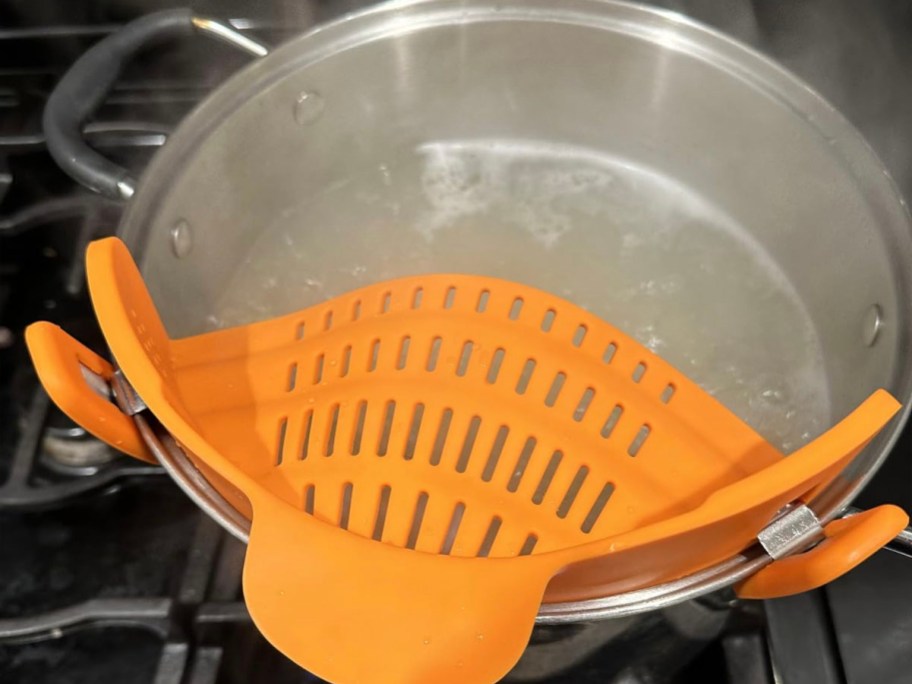 stainless steel pot boiling water on stove with orange strainer clipped on