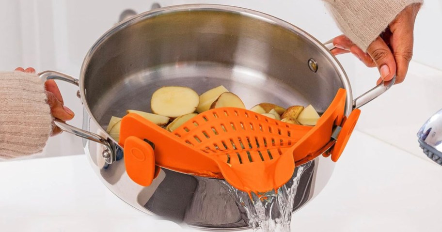 hands holding stainless steel pot with orange strainer on it