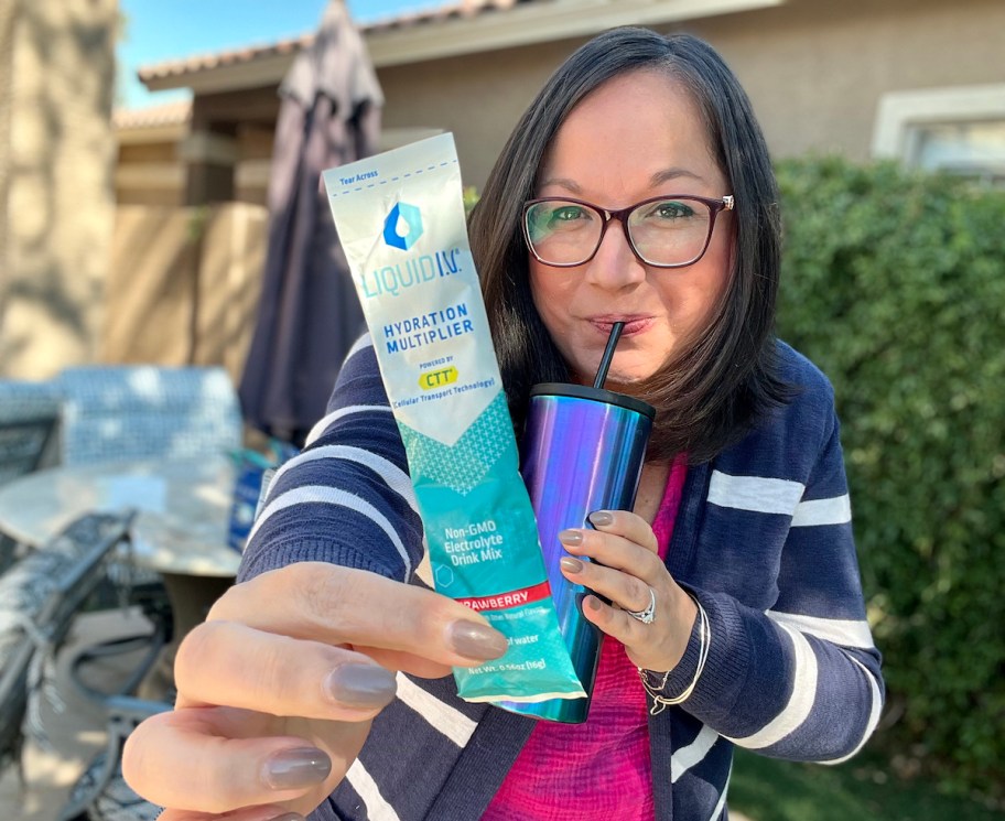 woman holding up a liquid iv pack while drinking water bottle