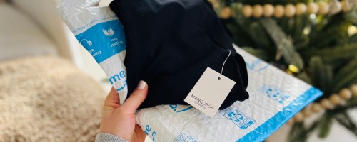 hand holding an amazon envelope bag and black mangopop bodysuit in front of christmas tree