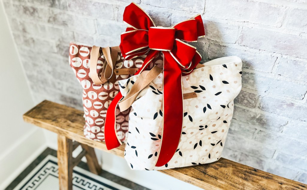 two canvas snap totes on wood bench with big red bow