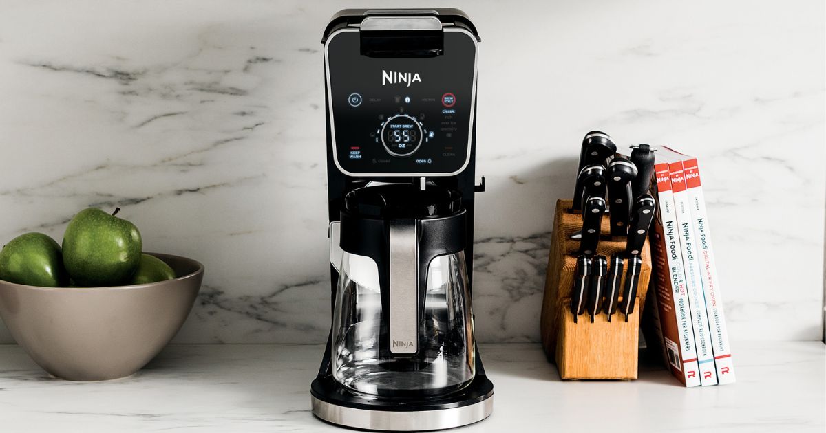 ninja coffee maker sitting on a counter near knives, books, and a bowl of apples