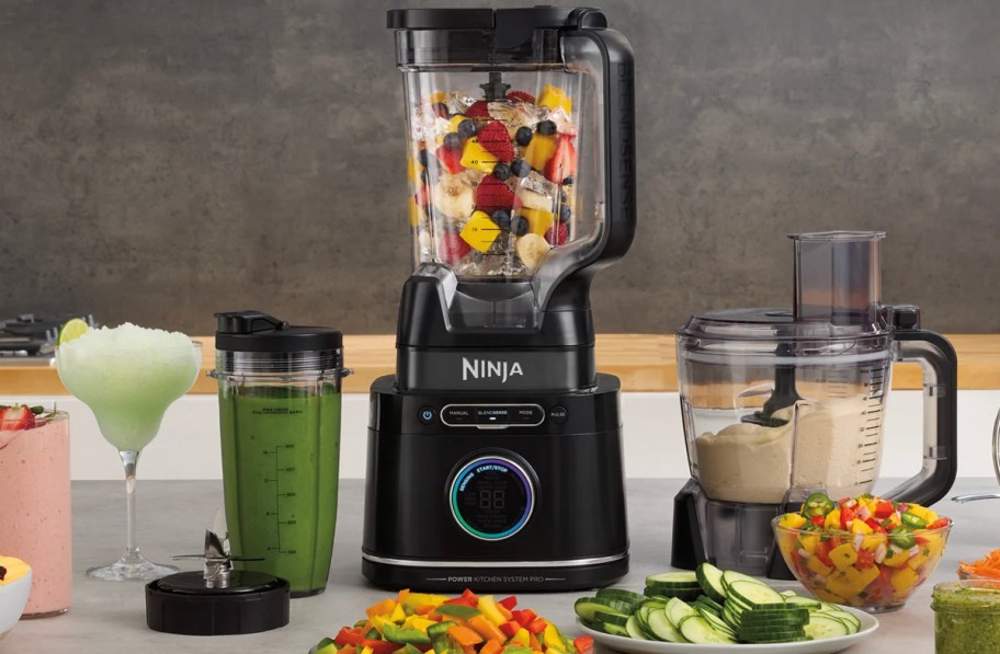 black ninja blender on table with cup full of smoothie and veggies in front on plates 