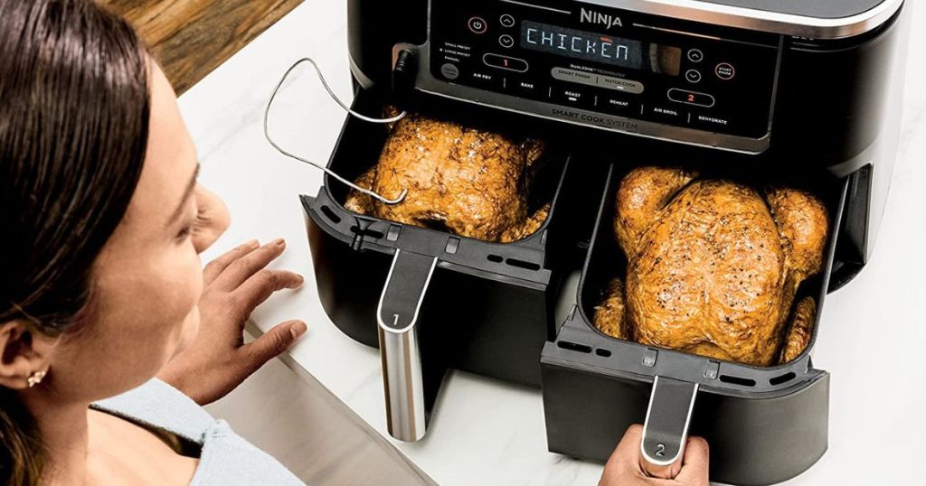 woman using Ninja Foodi Air Fryer with both baskets pulled out with whole chickens in each