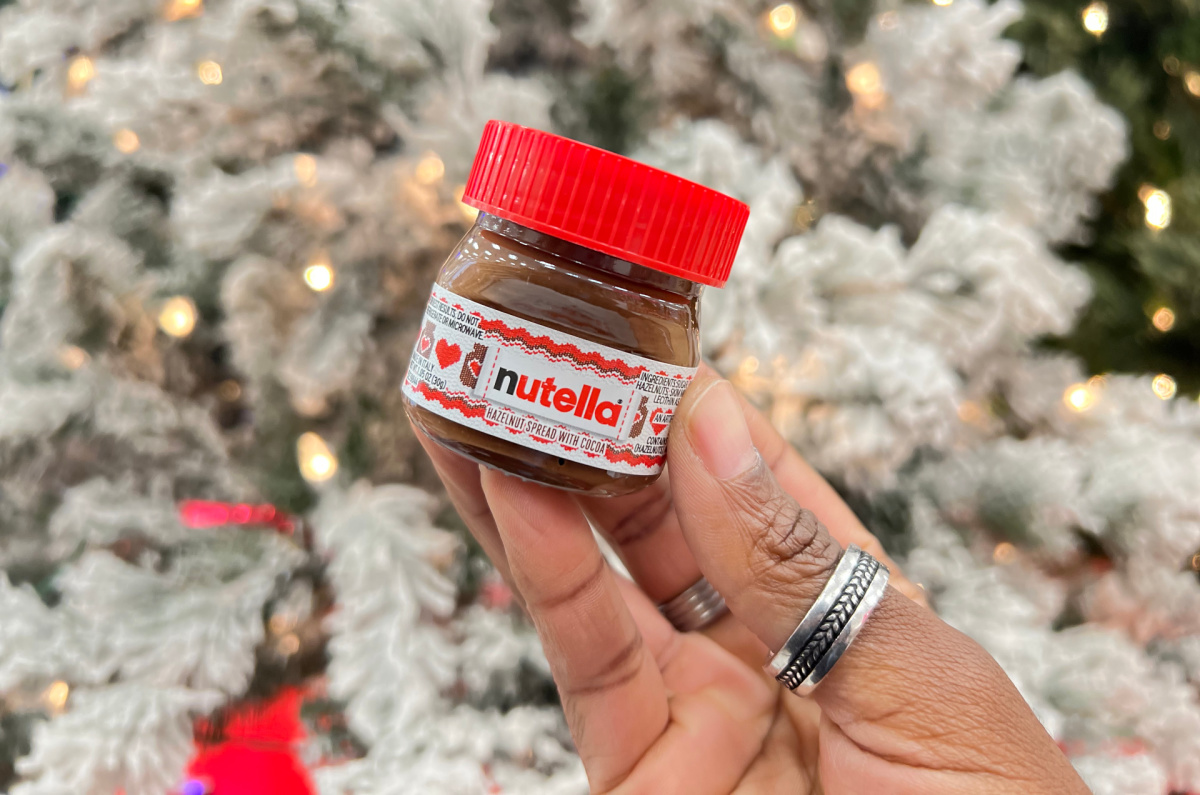 hand holding up a mini jar of nutella in front of a flocked christmas tree