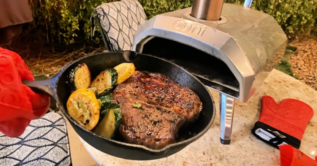 cast iron pan in front of ooni pizza oven holding steak and veggies