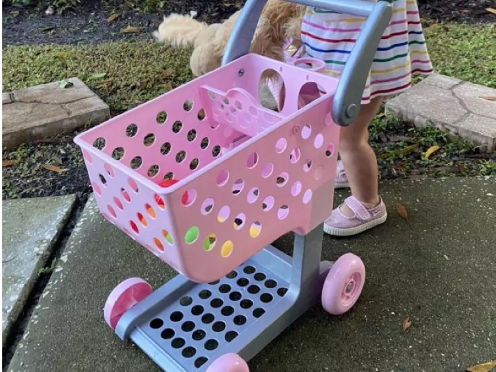little girl pushing a pink toy shopping cart