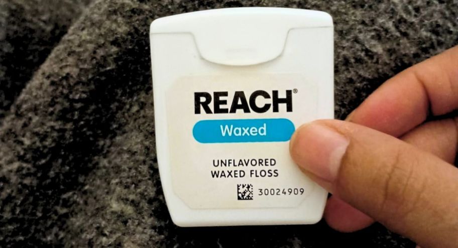 a mans hand holding a box of reach unflavored waxed dental floss
