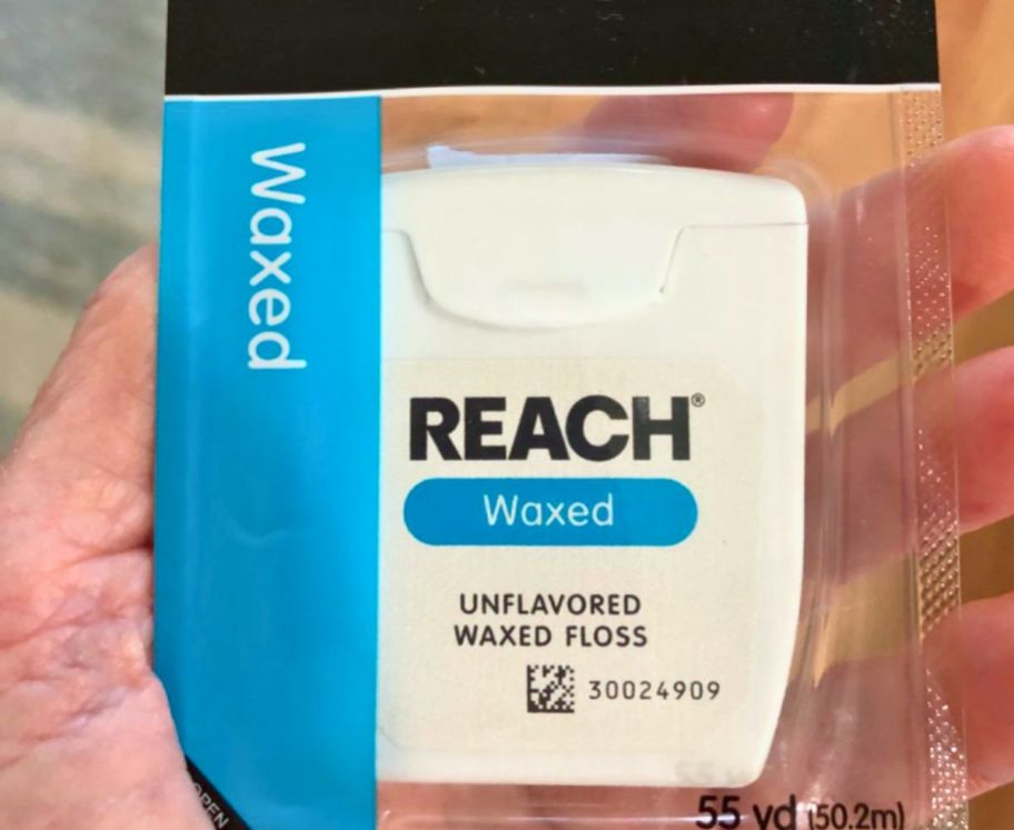 a mans hand holding a box of reach unflavored waxed dental floss