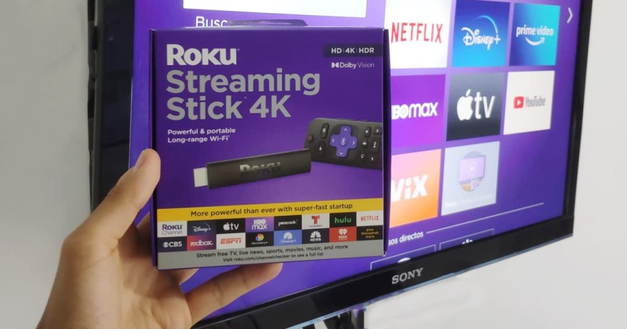 person holding roku box in front of tv