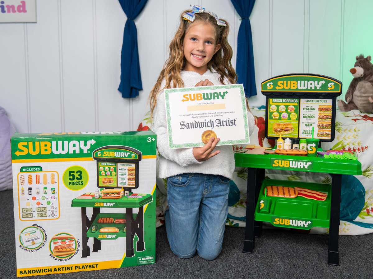 girl with a certificate posing next to a subway playset