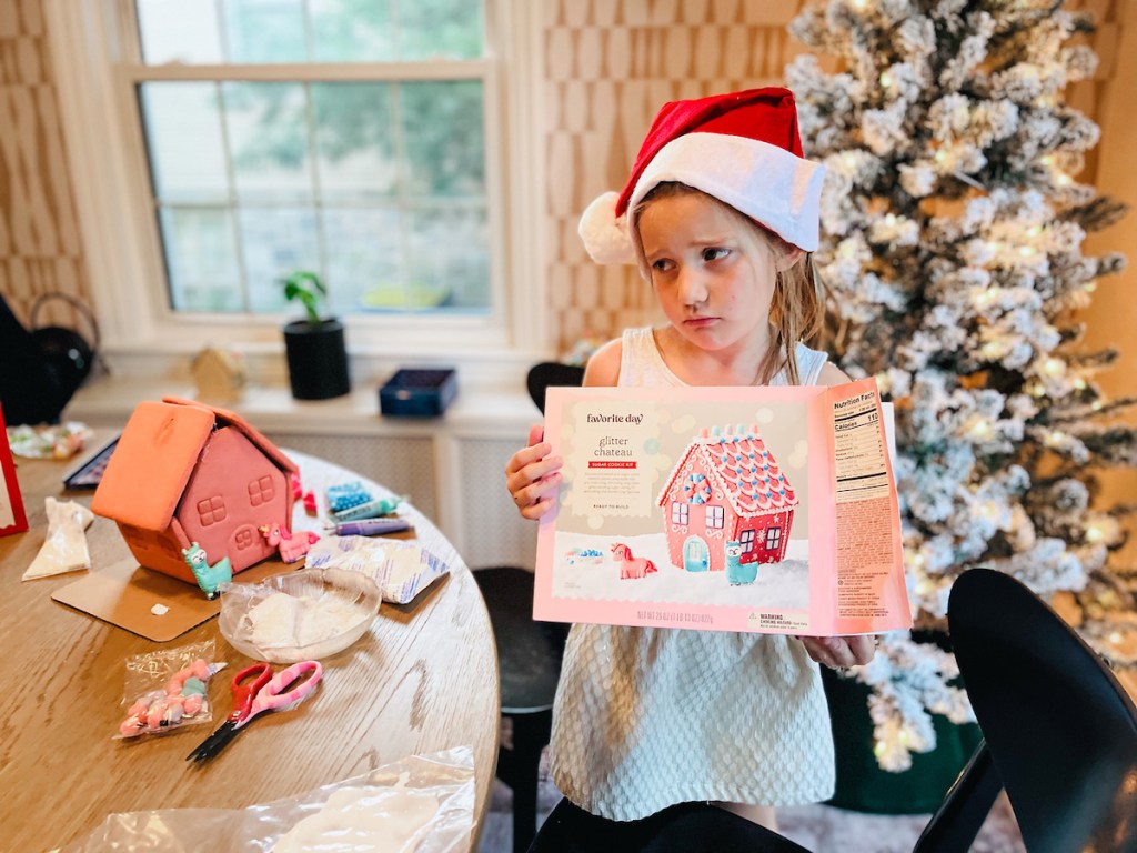 girl holding pink gingerbread house box looking sad